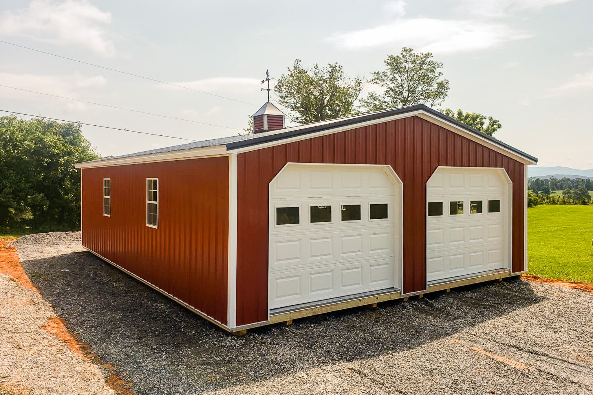 One of our storage buildings for sale in Salem - red and white double garages in Salem VA - Red metal siding with double overhead doors on short side - two white-framed windows on long side - red and white cupola with weather vane on black metal roof