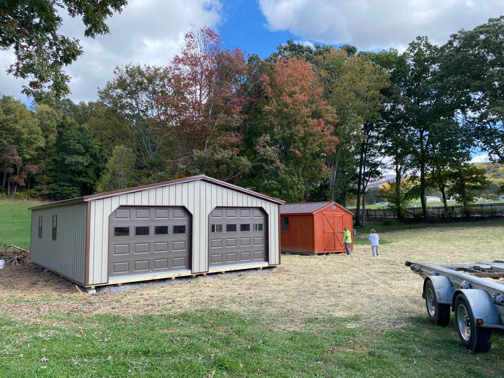 a two car modular garage just finished being delivered in a grassy field with early autumn trees in the background.