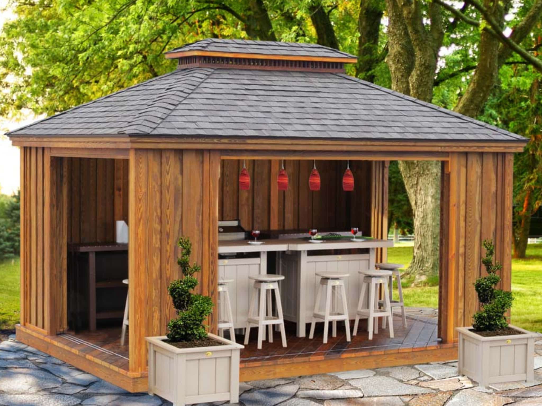One of our brown wooden gazebos - Featuring white oblong table and several matching stools - lush green trees in background