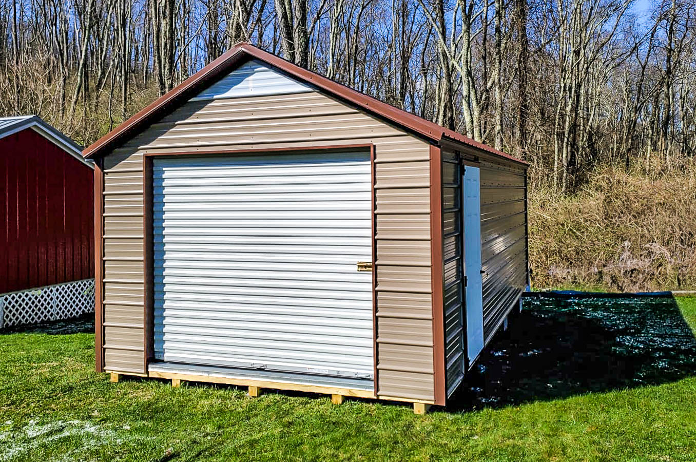 Budget shed with beige metal siding, brown trim, and a white roll-up garage door placed on a grassy yard.